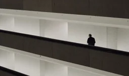 a man walking along dark walkways in a white building 